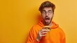 Young amazed man wear orange sweatshirt casual clothes eat fast food burger drink soda pop cola water isolated on plain yellow background.
