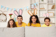 Happy family in bunny ears behind sofa at home on Easter Day