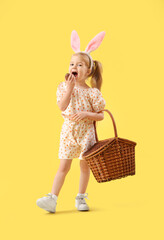 Sticker - Cute little girl in bunny ears with basket eating chocolate Easter egg on yellow background