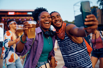 Wall Mural - Cheerful black couple taking selfie on summer music festival.