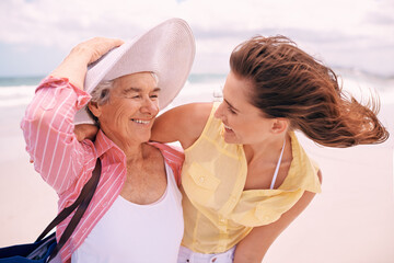 Wall Mural - Senior, mother and woman with beach wind or vacation bonding on tropical island or holiday, happiness or retirement. Old person, daughter and hat at Florida seaside or travel tourism, relax or trip