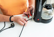 © Artsaba Family - Person in orange shirt cutting coffee maker s power cord with pliers, promoting electrical safety.