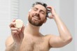 © New Africa - Happy man showing solid shampoo bar in bathroom, selective focus