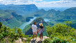© Fokke Baarssen - Panorama Route South Africa, Blyde river canyon with the three rondavels, Asian women and Caucasian men on vacation in South Africa looking out over green mountains on a road trip