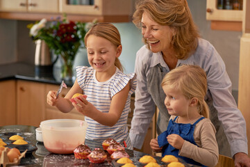 Mature woman, children and smile for baking in retirement for family, fun and bonding at home. Happy, female pensioner and girl with cupcake, laugh and icing for creative fun together in kitchen