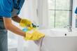 Focused on chores a woman in uniform sprays and cleans bathroom sink and faucet. Her dedication to housework emphasizes purity hygiene and shining fixtures at home. spray cleaner