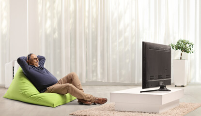 Poster - Mature man sitting on a green bean bag chair and relaxing in front of tv