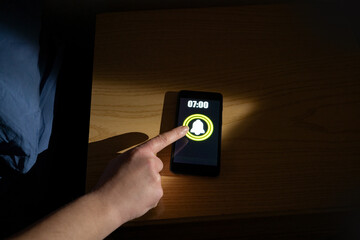 Close-up of a woman's hand waking up and turning off the alarm clock on the smartphone. Productive person ready start a day with business opportunities. Close-up focus on mobile phone clock showing