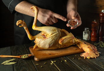 Chef preparing raw rooster in saloon kitchen. Before roasting, the cook adds spices to the rooster. Preparing to make an old-fashioned fried chicken recipe