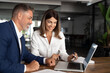 © Stock 4 You - Mature 40s age Latin business man mentoring mid age European business woman discussing project on laptop in office. Two colleagues, group of partners, businessman and businesswoman working together.