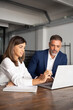 © Stock 4 You - Team of diverse partners sitting at table mature Latin business man and European business woman discussing project on laptop in office. Two colleagues of professional business people working, vertical