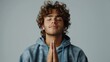 © Zaleman - A young Caucasian man claps his hands in hope. Standing in front of a white background, he closes his eyes, prays and smiles with a dreamy smile.