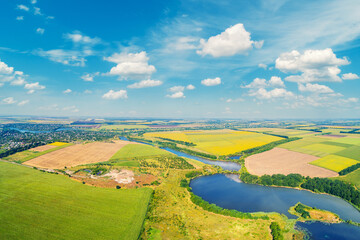 Wall Mural - Sunny day in the village. Rural landscape in daylight. Aerial view of a meandering river, cultivated fields, and a beautiful cloudy sky.