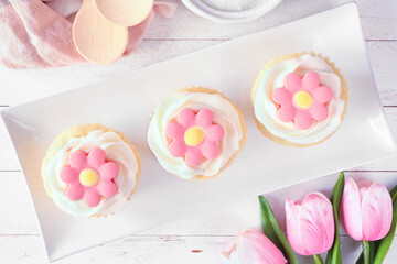 Wall Mural - Plate of pink spring flower cupcakes. Above view table scene with a white wood background.
