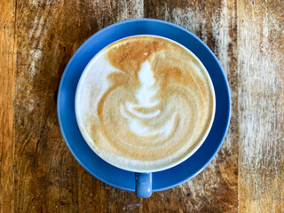 Coffee Art of latte with flower in foam in a blue mug and saucer on a wooden table