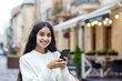 © Tetiana - Close-up photo of a smiling Indian woman standing outside, waiting to meet, walking down the street, holding a phone and looking at the camera