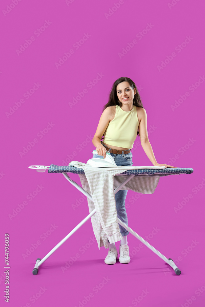 Pretty young woman ironing clothes on purple background