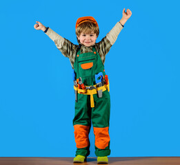 Wall Mural - Happy child boy in uniform and hard hat with toolbelt of toy tools for building. Cute kid repairman in protective helmet with builder tools set. Little child builder playing with toy tools for repair.