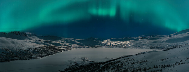 Wall Mural - Wide scenic night panorama of winter mountains highlighted by Aurora Borealis green lights. Norway Swedish Northern mountains area