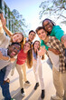 © CarlosBarquero - Vertical multiracial group of teenagers taking a selfie looking front camera laughing and having fun piggybacking together outdoor. Young students enjoying their free time with friends in street city