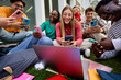 © CarlosBarquero - Group of cheerful young multiracial university students immersed on their mobile cell, technology addicted friends sitting outside university campus. Smiling gen z people concentrated using smartphone