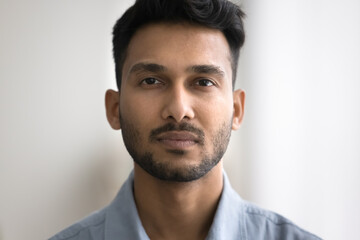 Close up of unsmiling Indian bearded guy standing indoor staring at camera. Man having attractive appearance, looks confident and serious. Millennial generation person, businessman head shot portrait