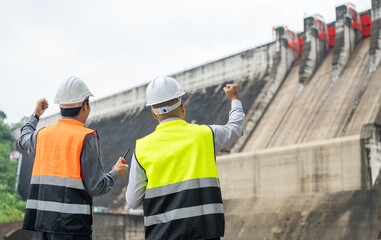 Confident asian two maintenance engineers man inspection discussstion with tablet at construction site dam with hydroelectric power plant and irrigation. Team engineer man working at project