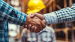 © apichat - Close-up of a firm handshake between two construction workers at a building site, representing a professional agreement.