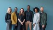© Shani work - A group of seven business professionals in a spacious office with a sky-blue background. They are all looking at the camera with optimistic smiles
