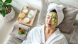 © john - Relax young Asian woman in bathrobe, towel on a head, lying on the sofa bed with sliced cucumbers on her eyes and beauty treatment items for spa procedures such as essential oil and salt massage.