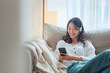 Happy asian woman listening to music from mobile phone while sitting on the the sofa at homes, Smiling girl relaxing with headphones in morning, Time to relax. copy space.
