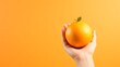 A hand holding an orange against orange gradient background