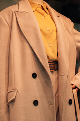 Wall Mural - Close up details of a beige long coat and a bright yellow shirt. Casual stylish women's fashion