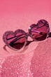 Sunglasses heart shaped on a pink sand background with glitter and sparkle. Summer aesthetic visual concept.	