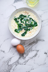 Wall Mural - Bowl of stracciatella soup with spinach on a white marble background, vertical shot with space, view from above