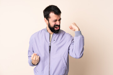 Caucasian man with beard wearing a jacket over isolated background celebrating a victory