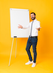 Wall Mural - Full-length shot of businessman giving a presentation on white board over isolated yellow background presenting and inviting to come with hand