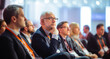 © Darya - A group of professionals sitting in a row at a conference or seminar. They are dressed in business attire, focusing attentively on something off-camera.