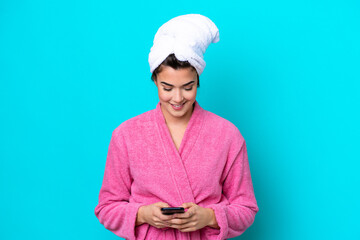 Wall Mural - Young Brazilian woman with a bathrobe isolated on blue background sending a message with the mobile