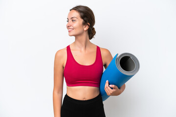 Wall Mural - Young sport caucasian woman going to yoga classes while holding a mat isolated on white background looking side