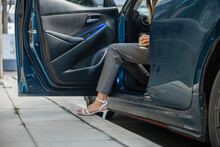 In A City Setting A Businesswoman In A Stylish Suit Sits In A Luxury Car. Her Slender Leg Clad In High Heels Gracefully Opens Door Showcasing The Blend Of Modern Transportation And Corporate Glamour.