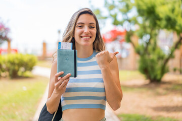 Canvas Print - Young pretty woman holding a passport at outdoors pointing to the side to present a product