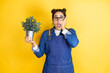 Young caucasian gardener woman holding a plant isolated on yellow background afraid and shocked, surprise and amazed expression with hands on face