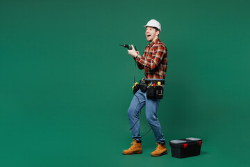 Poster - Full body young employee laborer man wear red shirt hardhat hat use hold electric drill isolated on plain green background. Instruments accessories for renovation apartment room. Repair home concept.