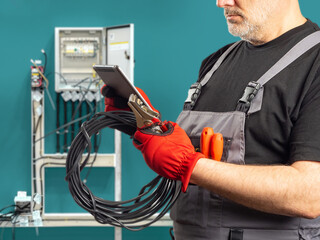 Wall Mural - High voltage wire in hands of electrician. Man near power shield. Cropped electrician using electronic tablet. Electrician preparing for electrical installation work. Man electrification specialist