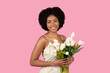 Warmly smiling young woman with natural afro hair lovingly holding a bouquet