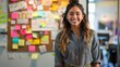 Smiling young professional woman in front of a creative brainstorming board full of colorful notes, ideal for business and startup themes.