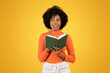 © Prostock-studio - Inquisitive young woman with afro hair, in orange turtleneck, pensively holding a green book