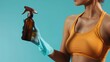 A focused individual, clad in a sporty tank top and medical gloves, meticulously holds a spray tan bottle, ready to apply for an even, flawless finish against a turquoise backdrop