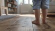 © Emi - Baby feet doing the first steps. Baby's first steps. Child's bare feet on a wooden floor in front of a window. A lonely kid standing in front of a window in the room in the morning. Generative ai